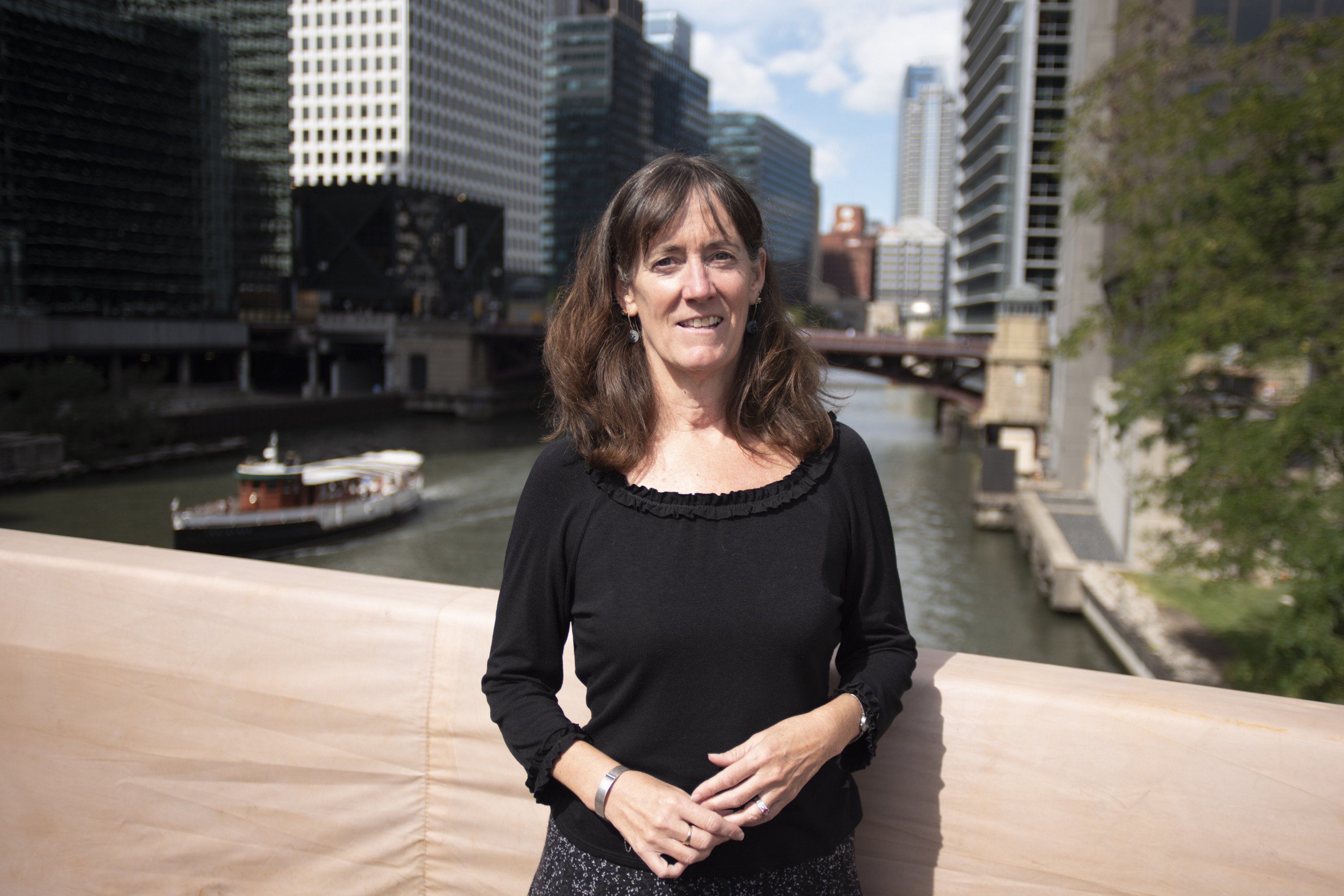 Margaret Frisbie, executive director of Friends of the Chicago River, stands on a bridge in Chicago with the downtown and river behind her.