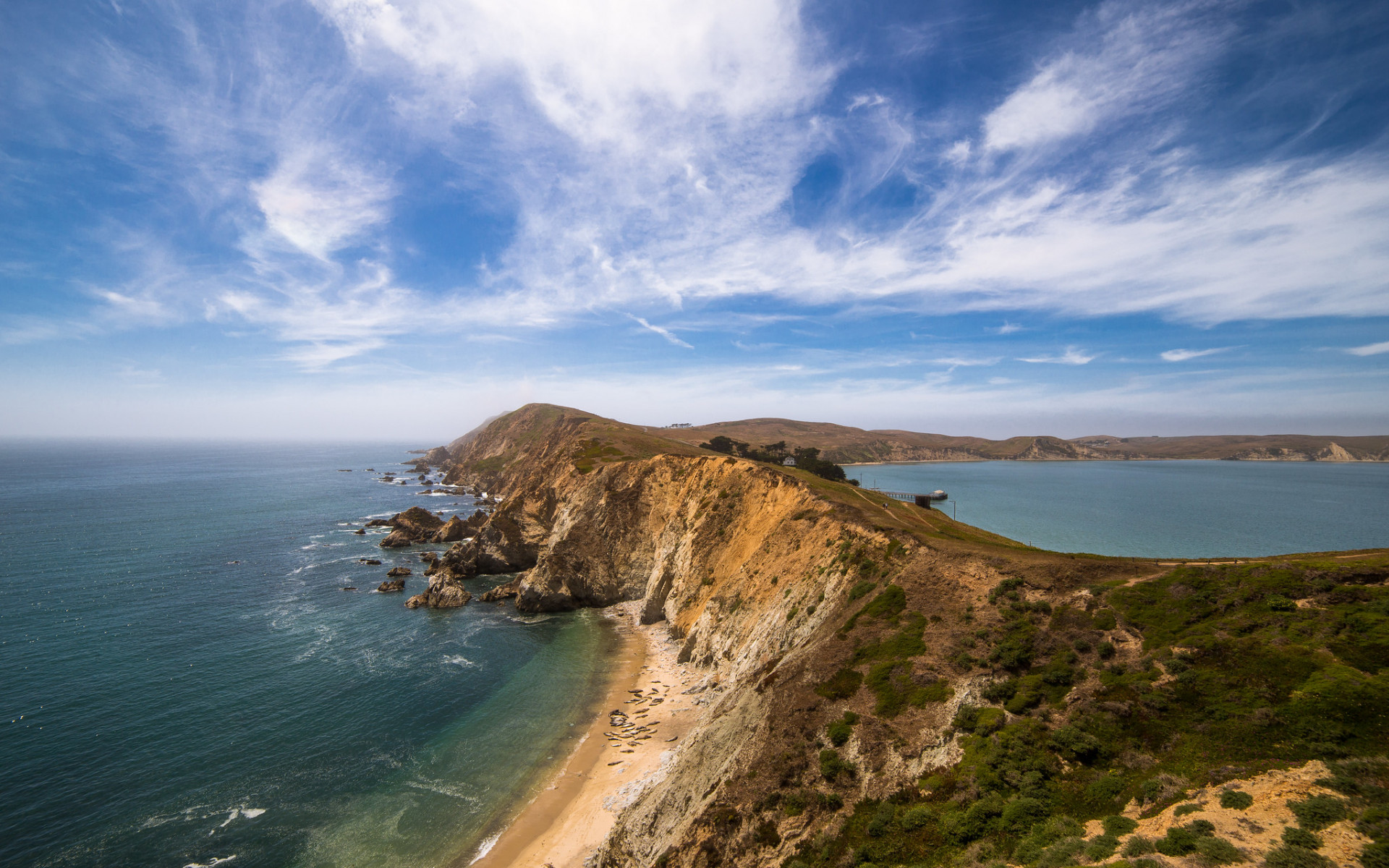 A wide landscape of the Point Reyes National Seashore. A steep, thin peninsula is flanked on both sides by deep blue waters.