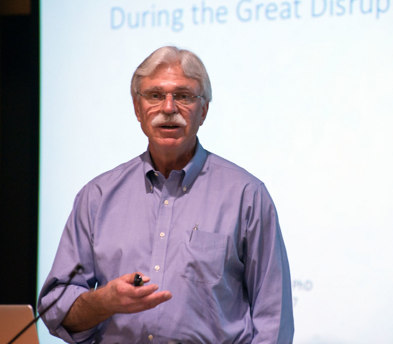 Stephen Mulkey, who discusses divesting from fossil fuels in the podcast, wears a purple button down shirt and stands in front of a projected presentation.