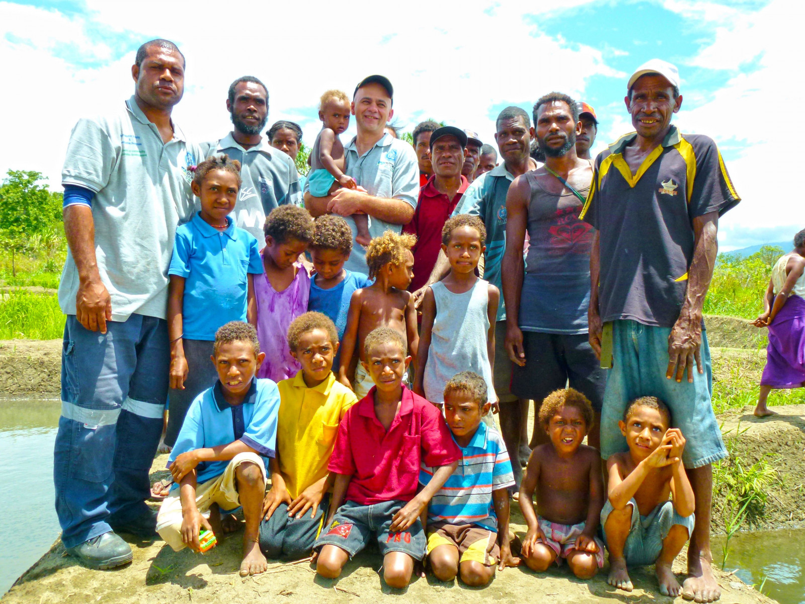 Jesmond Sammut stands with several villagers and their children. Jes has helped teach these farmers aquaculture, or fish farming. 