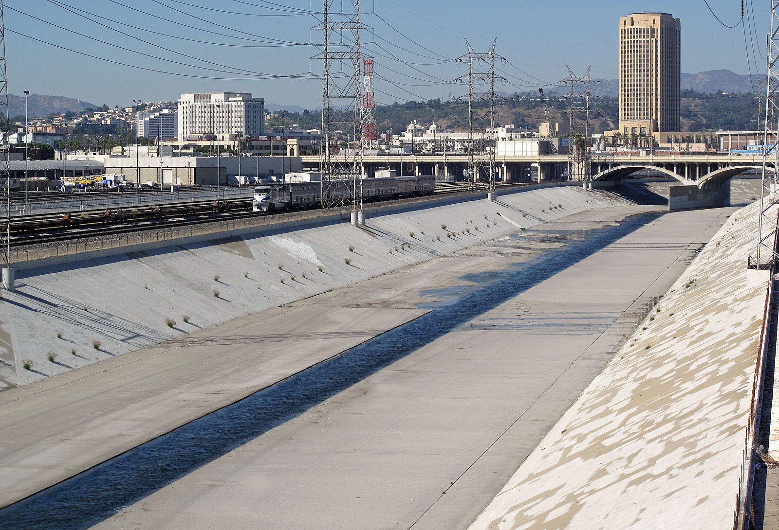 A concrete canal with a small stream of water flows through an urban area.