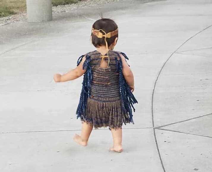 A small child wears traditional garb while walking outside. 