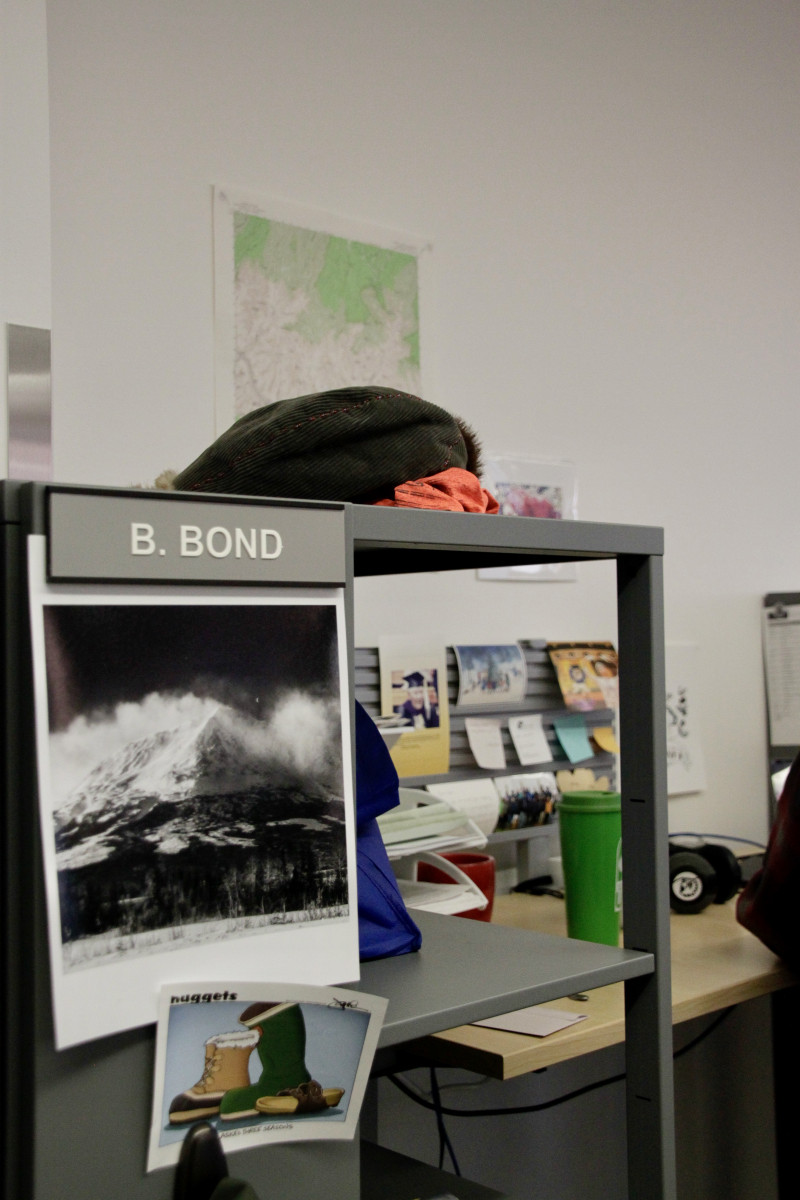 A close up image of Bond's workstation. A printout of a mountain enshrouded in clouds hangs from a shelf.