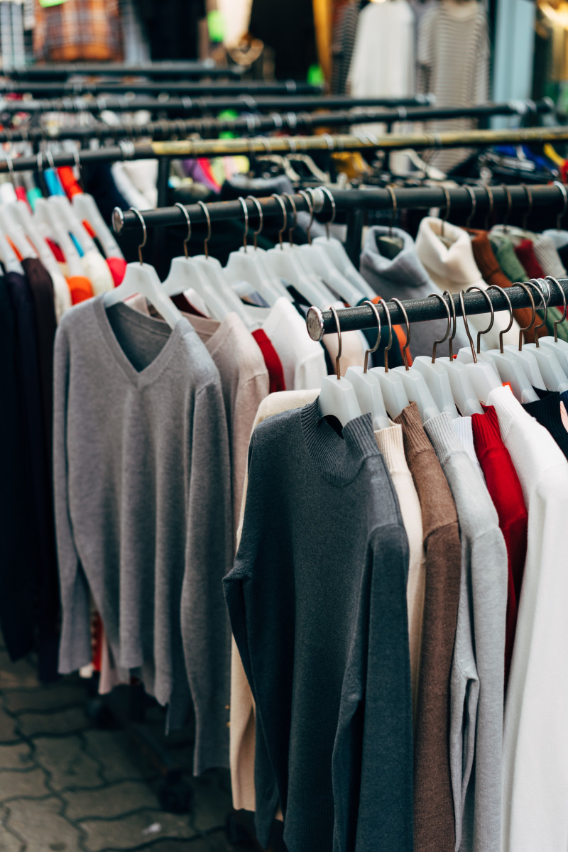 Rows of used clothes line the interior of a store where people go thrifting. 