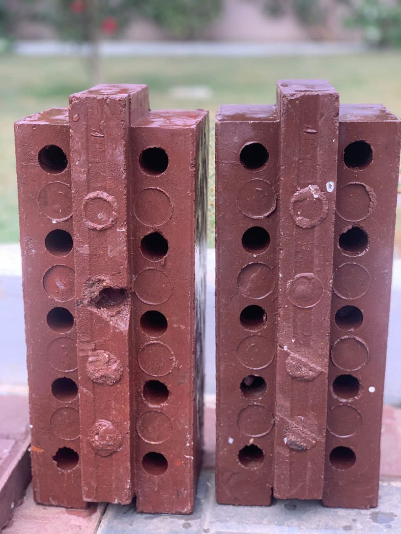 A red-colored recycled plastic brick with a ridge jutting out of the center to make them interlocking