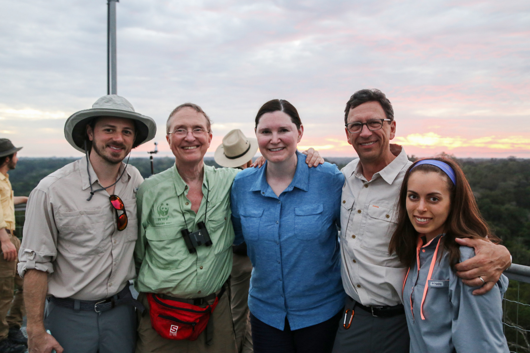 A line of five people stand with a sunrise in the background.