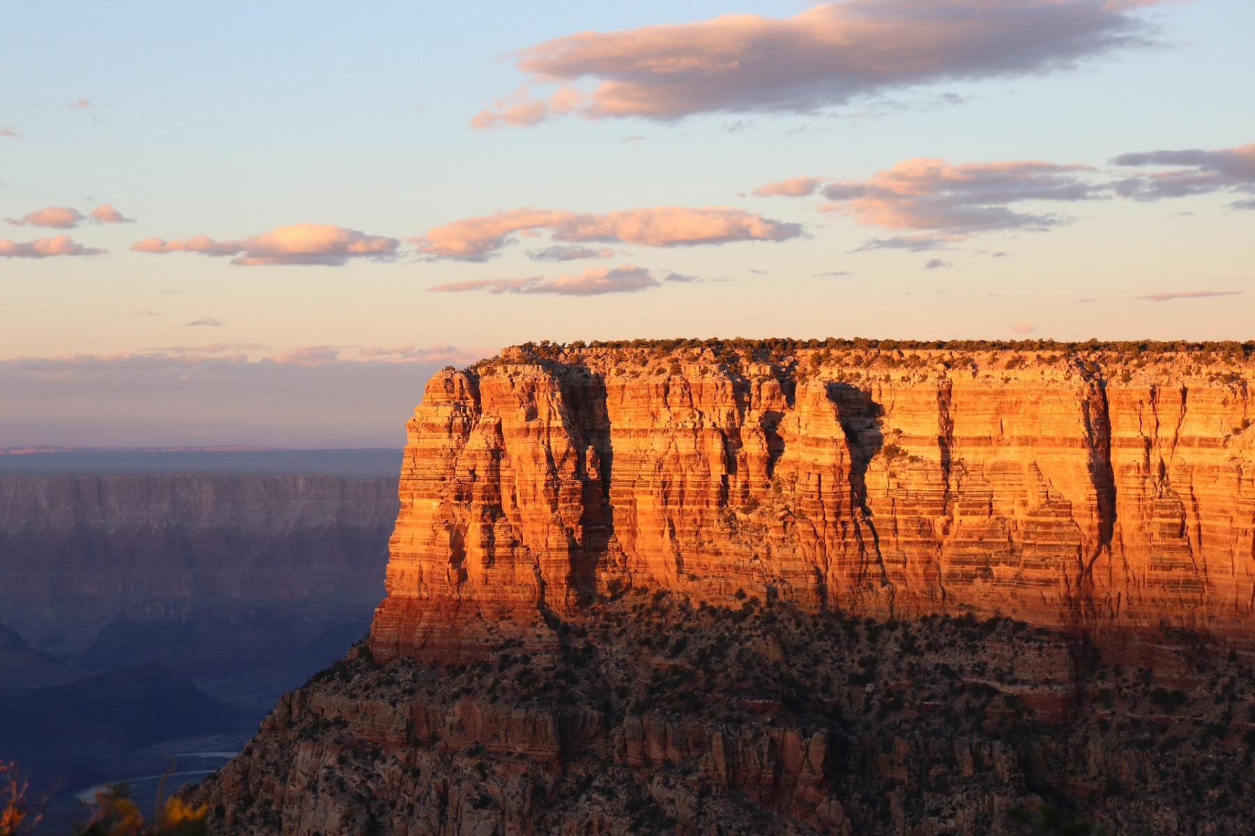 Light of a setting sun shining on a a striated canyon against a blue sky with fluffy clouds.