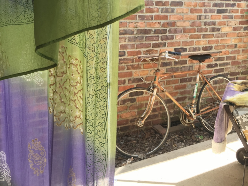 Looking out a window at an old bike leaning against a brick wall.