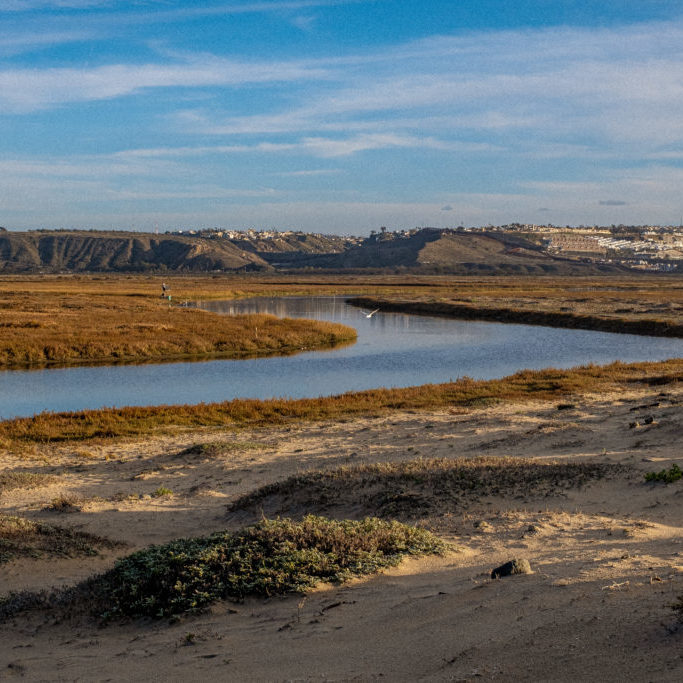 Sandy marshland giving way to a winding river. Hills lie in the distance of the estuary.