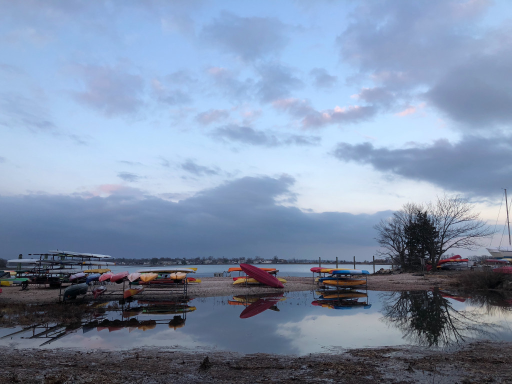 Dozens of kayaks lie on trailers in a partially flooded parking lot near the Long Island Sound.