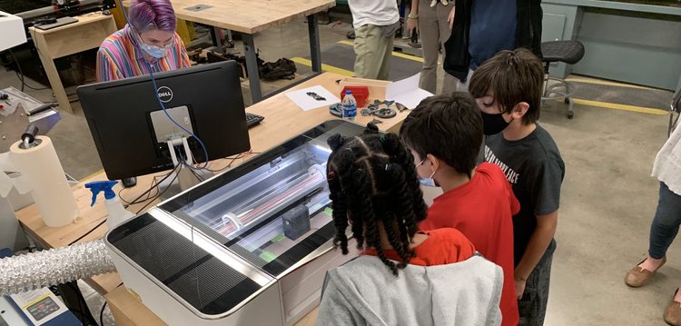 A small student group stands around a desk with a large printer on it.