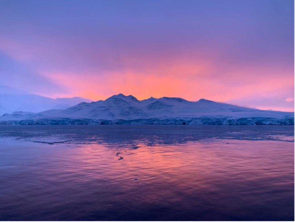 An orange and purple sunset behind a glacier in Antarctica